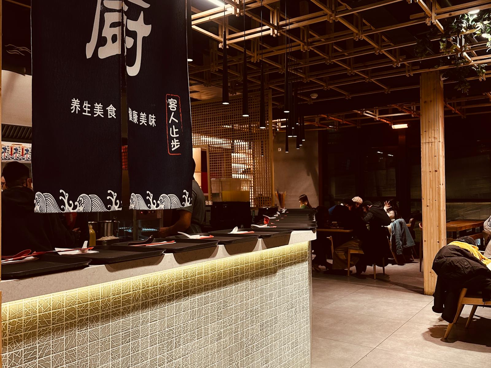 Interno di un ristorante sushi con banco, tavoli e illuminazione calda